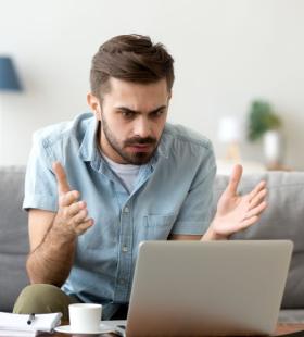 Man holding up hands in frustration in front of a laptop computer.