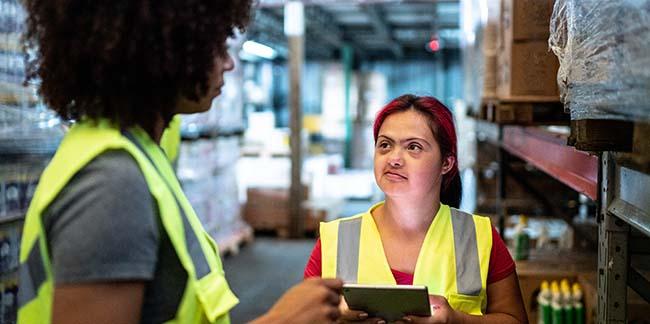 A woman with down syndrome working with a coworker in a warehouse