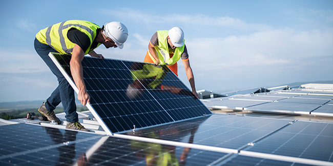 Workers in uniforms installing solar panels on a roof.